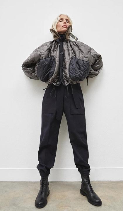 A model in an oversized black puffer jacket and trousers, shot against a plain wall