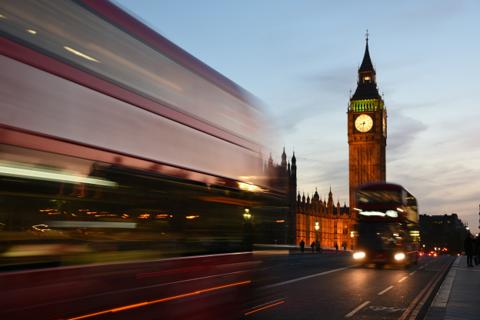 A red bus streaking past the Houses of Parliament at dusk