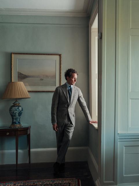 Man in a grey suit standing by a window in a panelled room