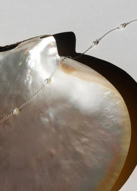 Fine chain necklace with pearls laid on a mother-of-pearl shell
