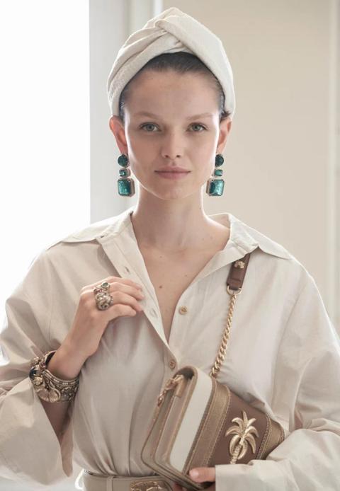 Model in a white turban and shirt with long emerald earrings and a gold bag