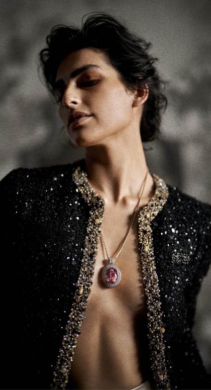 A model in a beaded jacket wearing a gemstone pendant