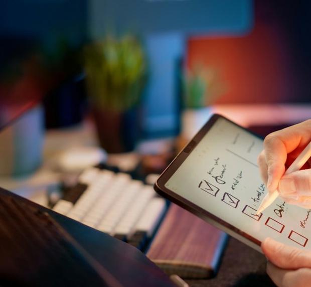 A hand ticking boxes on a checklist on a tablet, a keyboard beside it on the desk