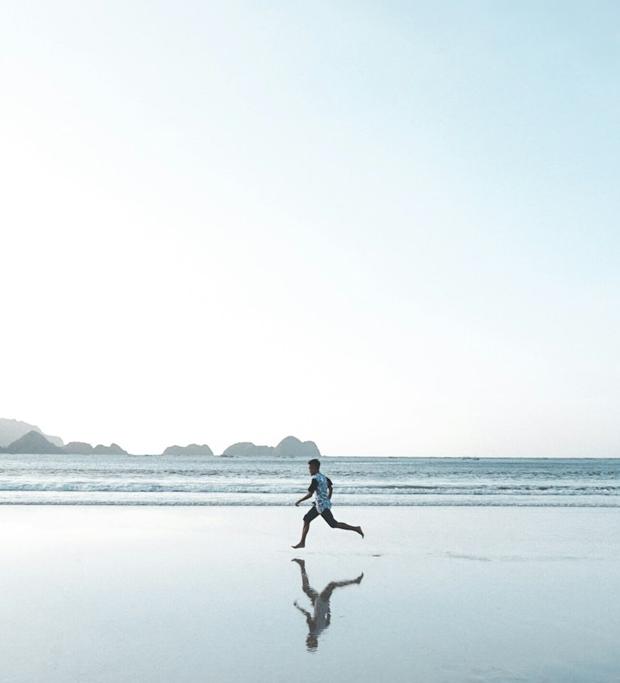 A person running along the edge of a calm sea on an empty beach in soft morning light