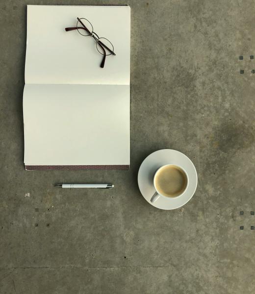 Un taccuino, degli occhiali e una tazza di caffè su una scrivania in cemento