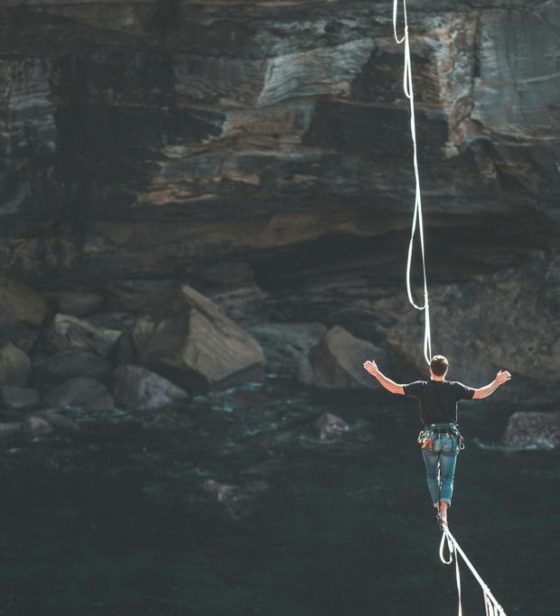 A slackliner crossing a line strung high above a dark gorge